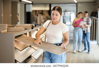 Young woman buyer chooses sample of laminate flooring in hardware store - Powered by Shutterstock