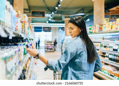 Young Woman Buying Beer Or Ale Alcohol In Liquor Store, Standing In Front Of Shelf, Holding Can Reading Label