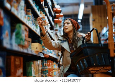 Young woman buying canned food at grocery store.