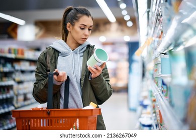 Young woman buying diary product and reading food label in grocery store. - Shutterstock ID 2136267049