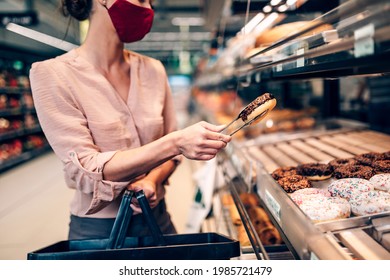 Young woman is buying freshly baked pastry in big modern bakery. She is wearing face protective mask due to Coronavirus epidemic. - Powered by Shutterstock