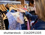 Young Woman Buying Used Sustainable Clothes From Second Hand Charity Shop Looking At Price Tag
