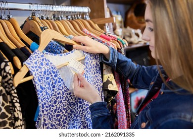 Young Woman Buying Used Sustainable Clothes From Second Hand Charity Shop Looking At Price Tag