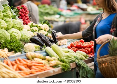 Young woman buying vegetable on stall at the market