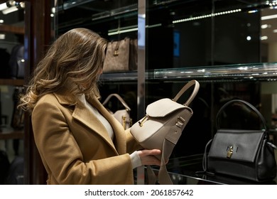 Young woman buys a bag in a boutique. Blonde in a beige coat. Luxurious expensive product. 