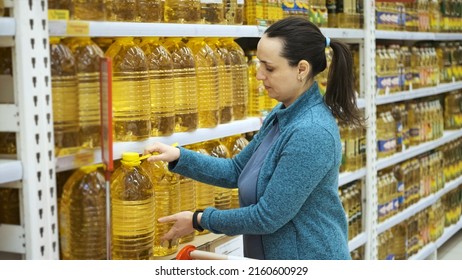 Young Woman Buys Big Bottles Of Sunflower Or Olive Oil In Grocery Store, Putting It Into Shopping Cart. Hoarding, Economic Crisis And Food Shortage