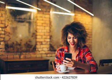 Young woman at cafe drinking coffee and using mobile phone
