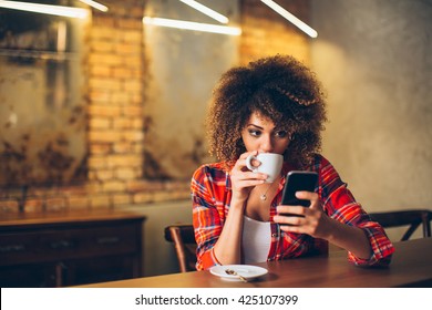 Молодая женщина в кафе пьет кофе и пользуется мобильным телефоном