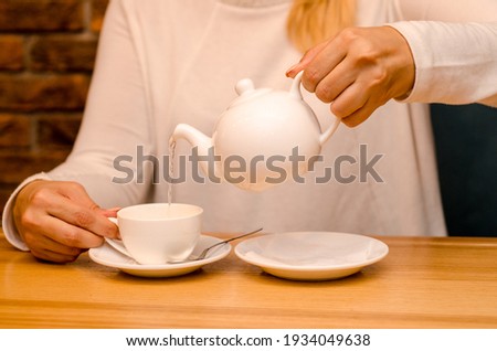 Young woman in a cafe drinks ginger tea and pours it from a teapot into a white cup on a saucer