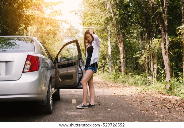 Young woman calling for assistance\
next to a broken down car parked on the side of a\
road