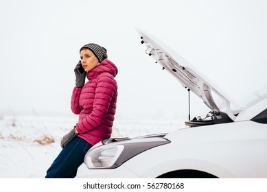 Young woman calling for help or assistance after her car breakdown in the winter. Broken down car with open hood on a country road. - Powered by Shutterstock