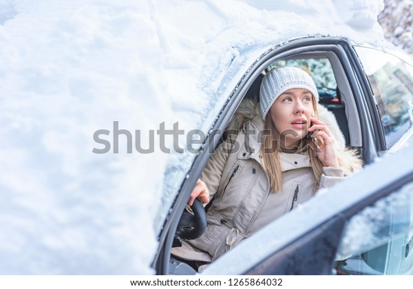 Young woman calling for help or\
assistance after her car breakdown in the winter. A woman calls for\
the breakdown services near her snow covered\
motorcar.