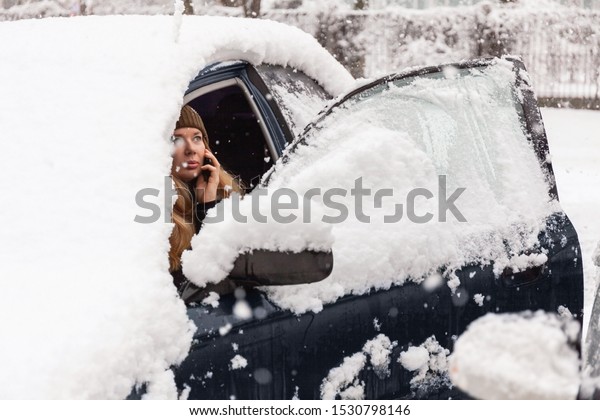 Young woman calling for help or assistance inside\
snow covered car.  Engine start in frost. Breakdown services in the\
winter.