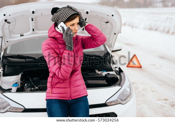 Young woman calling for help or assistance after
her car breakdown in the winter. Broken down car with open hood on
a country road.