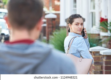 Young Woman Calling For Help On Mobile Phone Whilst Being Stalked On City Street By Man