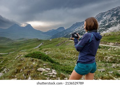Young woman with camera enjoying dramatic view of mountains of Durmitor, Montenegro on storm day - Shutterstock ID 2136529789