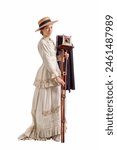 Young woman with camera wearing a beige vintage 1880s dress and straw hat isolated on white