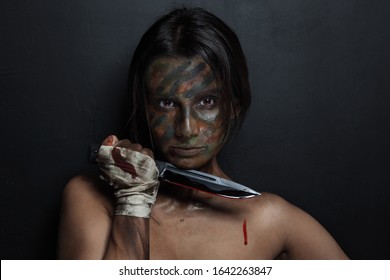 Young Woman With Camouflage Face Paint And Knife In Her Hand