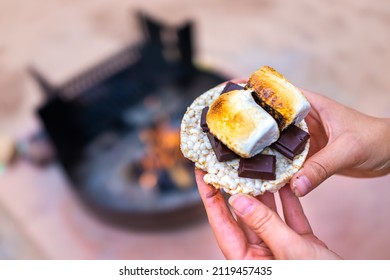 Young Woman Camping Closeup Hand Holding Roasted Marshmallows Smores With Chocolate Bar Squares And Rice Cake Cracker By Fire Pit In Campground Campfire Grill