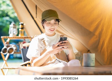 A young woman camping and operating a smartphone in a tent - Powered by Shutterstock