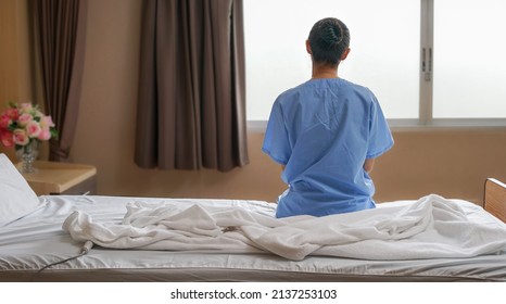 Young woman cancer patient sitting alone on a hospital bed is distraught sadly looks out the window with sick thoughtfulness. Chemotherapy and convalescence in recuperation release suffering from ill. - Powered by Shutterstock