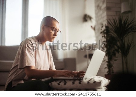 Young woman with cancer working on laptop, cancer awareness concept. Female cancer patient working from home, remote job, homeoffice.