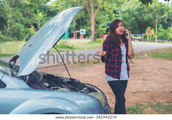 Young woman with car breaks down and she is\
calling the emergency services.\
