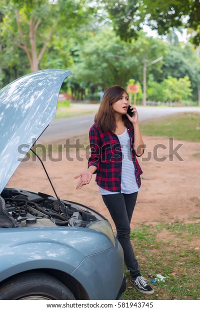 Young woman with car breaks down and she is\
calling the emergency services.\
