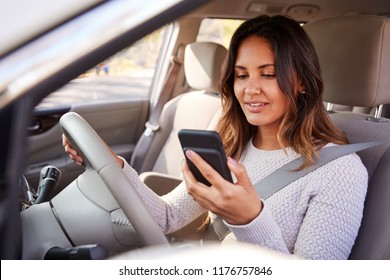 Young woman in car checking her smartphone while driving