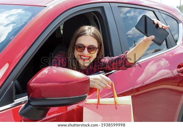 Young woman\
in car with colourful paper bags and phone. Girl driving a car. \
Smiling young woman sitting in red\
car