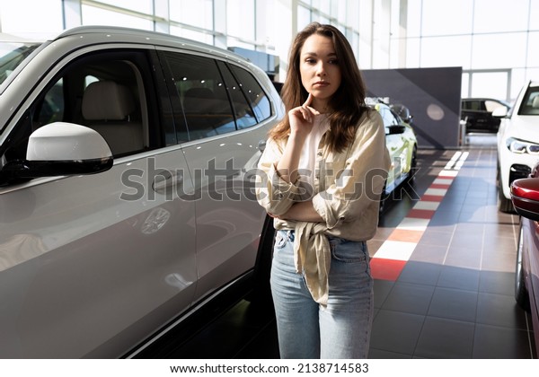young woman in a car dealership showroom puzzled by\
the choice of a new car