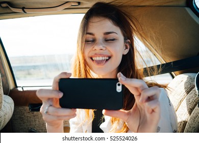 Young Woman In The Car Going On Holiday As A Passenger Makes Selfie. Photographed On A Mobile Phone