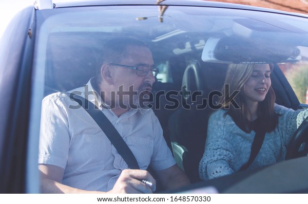 Young Woman in the car on\
driving test. Pretty teenage girl in Driving school. Student driver\
taking driving class. Look through windshield of the\
vehicle