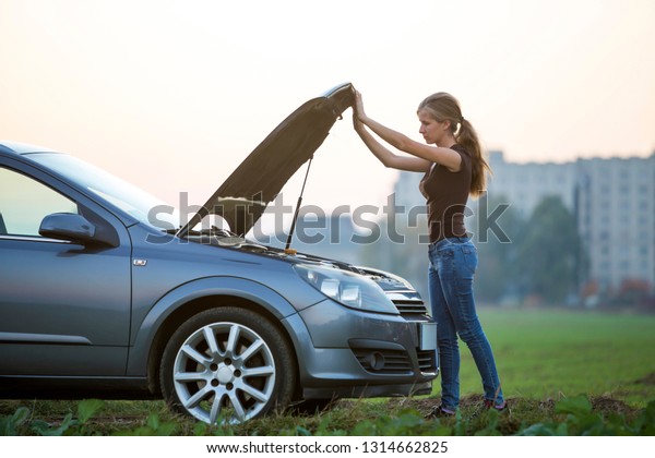 Young woman and a car with popped\
hood. Transportation, vehicles problems and breakdowns\
concept.