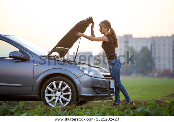 Young woman and a car with popped\
hood. Transportation, vehicles problems and breakdowns\
concept.