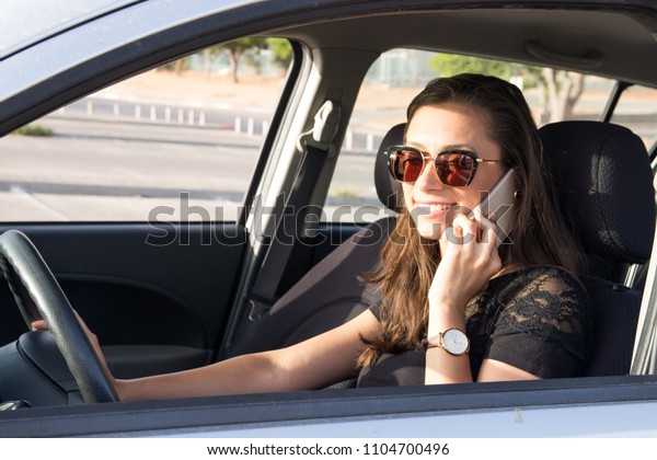 A young woman in the car talks on the smart phone\
and drives