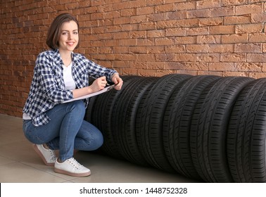 Young woman with car tires and clipboard near brick wall