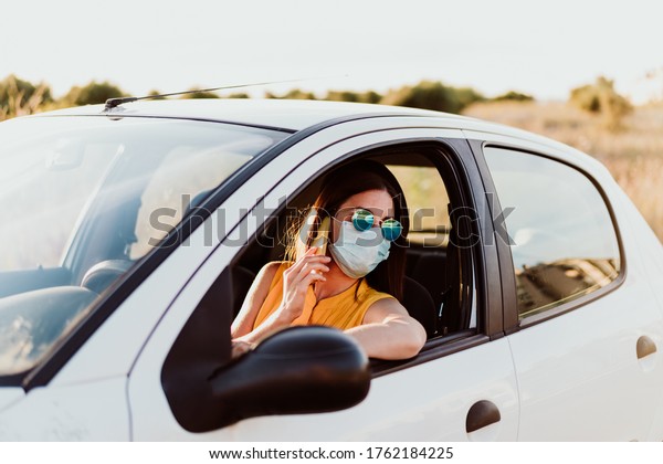 young woman in a\
car using mobile phone, wearing protective mask. Summer season.\
prevention corona virus\
concept