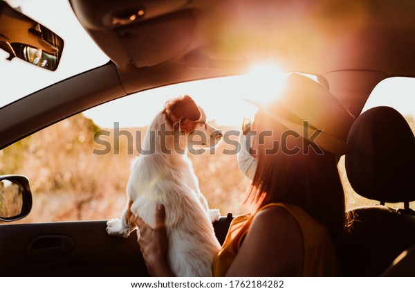 young\
woman in a car wearing protective mask, cuddling her cute small\
dog. Summer season. prevention corona virus\
concept