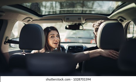 Young woman in a car,female driver looking at the passenger and smiling.Enjoying the ride,traveling,road trip concept.Driver feeling happy and safe.Learning how to drive,getting drivers licence.