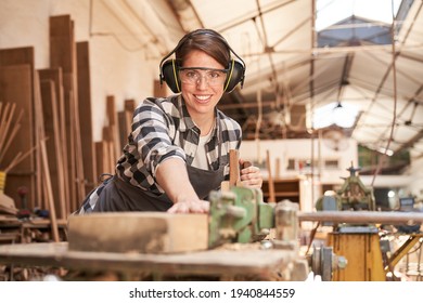 Young Woman As A Carpenter Apprentice While Planing Wood In The Carpentry Workshop