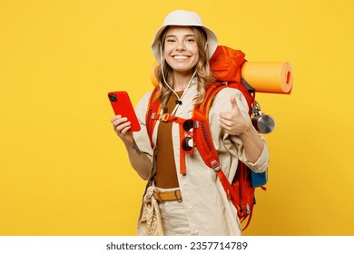 Young woman carry backpack with stuff mat use mobile cell phone show thumb up isolated on plain yellow background Tourist leads active lifestyle walk on spare time Hiking trek rest travel trip concept - Shutterstock ID 2357714789