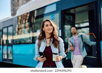 Young woman carrying coffee to go and mobile phone while getting of a bus at the station. - Powered by Shutterstock