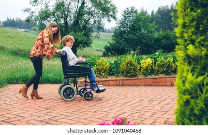 Young woman carrying her mother in a wheelchair through the garden