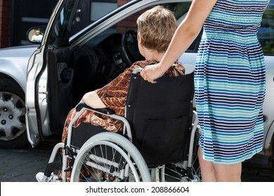 A Young Woman Is Carrying An Old Lady In A Wheelchair To The Car