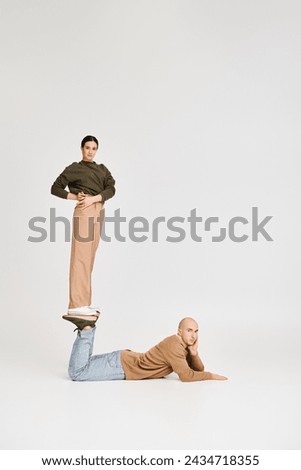 young woman in casual attire balancing on legs of man in a playful pose in studio on grey backdrop