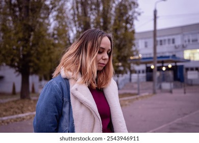 Young woman in casual attire stands in an urban park during early evening, surrounded by tall buildings and autumn trees. - Powered by Shutterstock