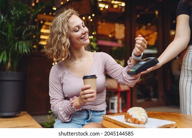 Young woman in casual clothes at cafe buy breakfast sit at table hold wireless bank payment terminal smart watch to process acquire payments drink coffee relax in restaurant during free time indoors.