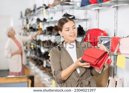 Young woman in casual clothes chooses leather handbag in shoe store..