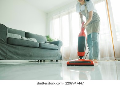 Mujer joven vestida de manera informal, limpiando el suelo usando aspiradora y equipos de limpieza en la sala de estar en casa. Concepto de limpieza.